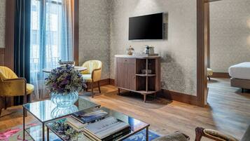 Een moderne woonkamer met een glazen salontafel, een gele fauteuil, een houten kast en een flatscreen televisie aan de muur.