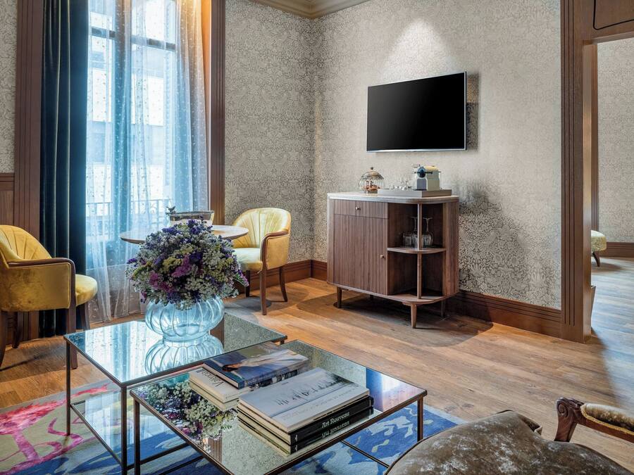 Een moderne woonkamer met een glazen salontafel, een gele fauteuil, een houten kast en een flatscreen televisie aan de muur.