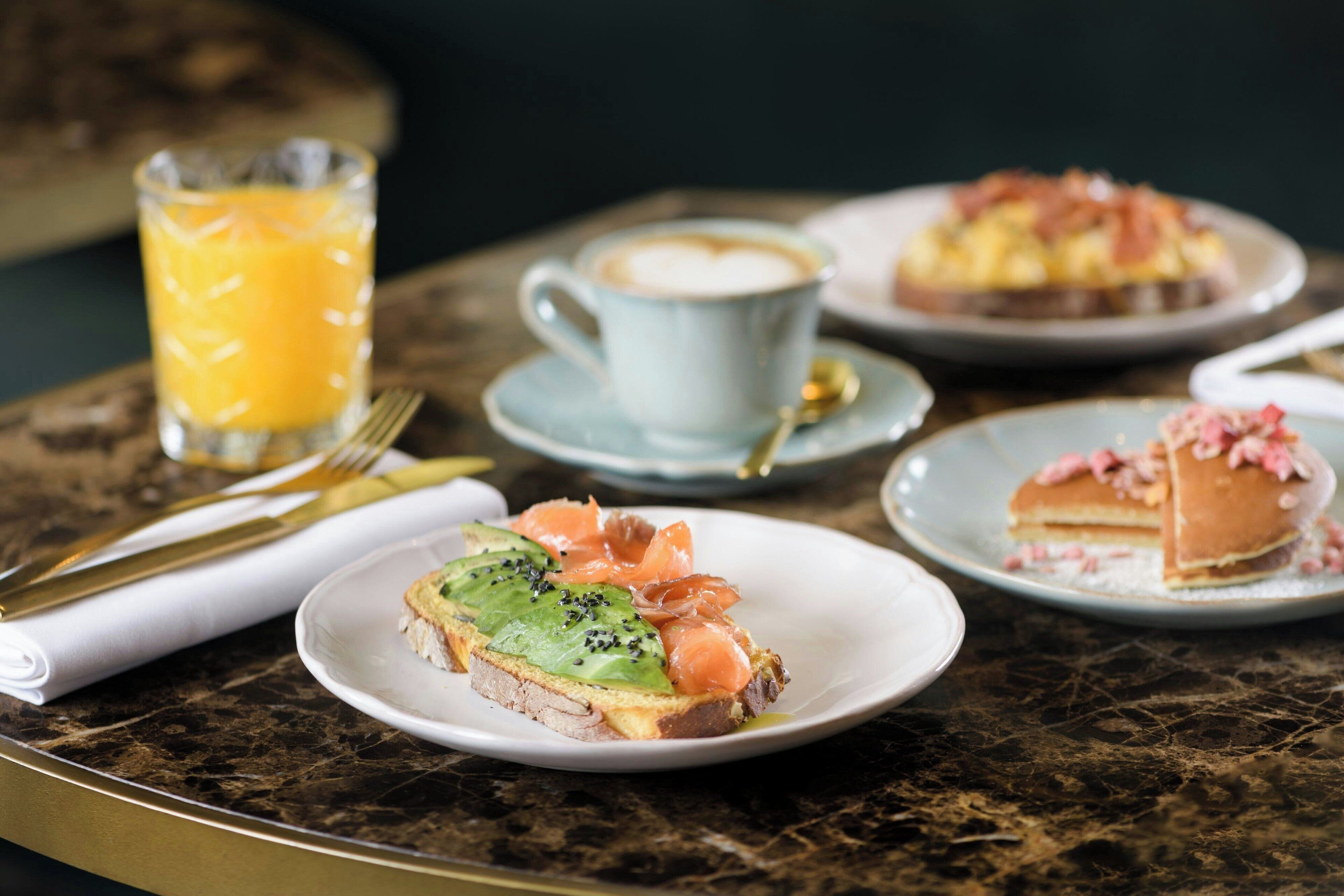 Un desayuno con tostadas, salmón y una taza de café sobre una mesa de mármol.