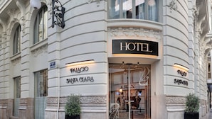 A hotel facade with "HOTEL" signage, "PALACE" and "SANTA CLARA" names, and two potted plants.