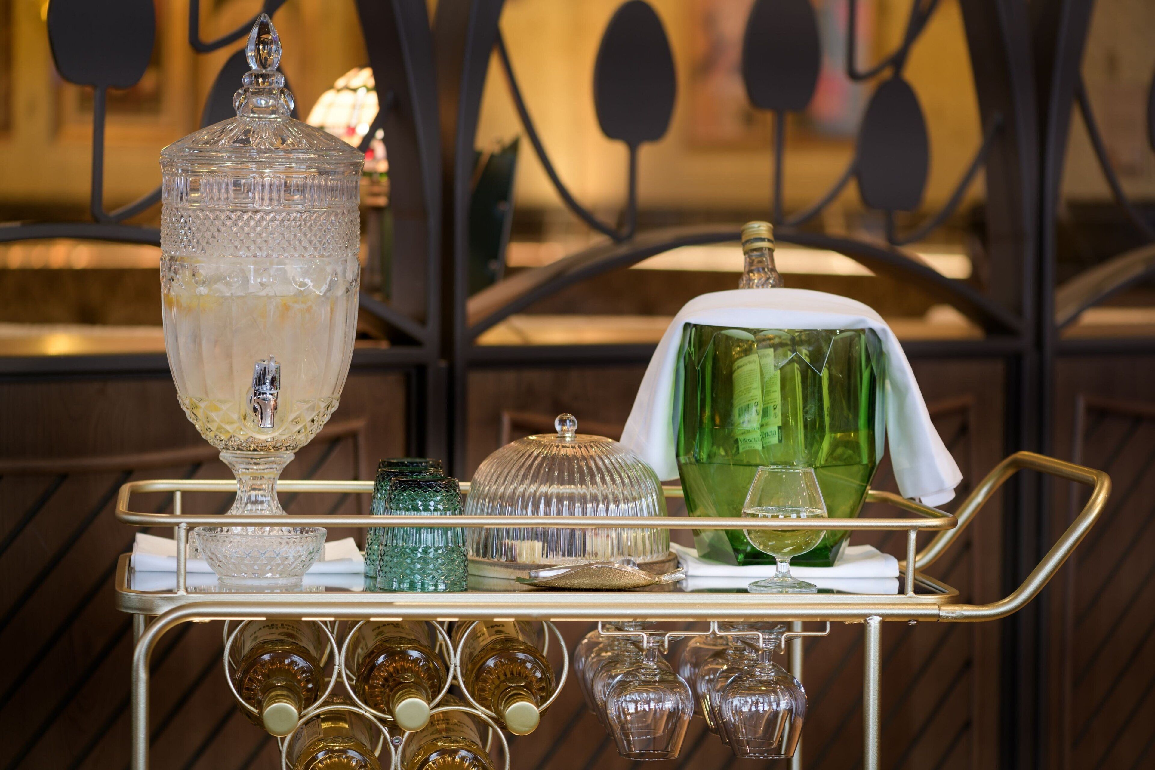 A bar cart with a large crystal decanter, a green bottle, and various glasses.