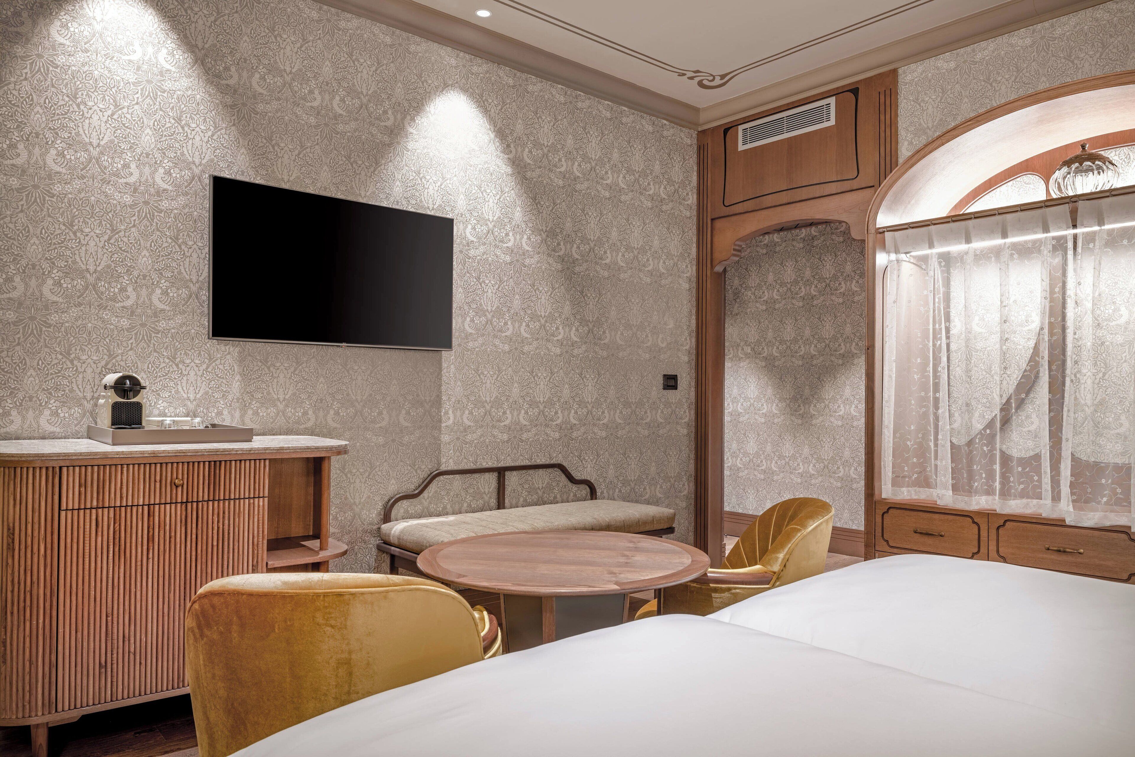 A hotel room with a large bed, a wooden vanity, a round table, and a TV mounted on the wall.