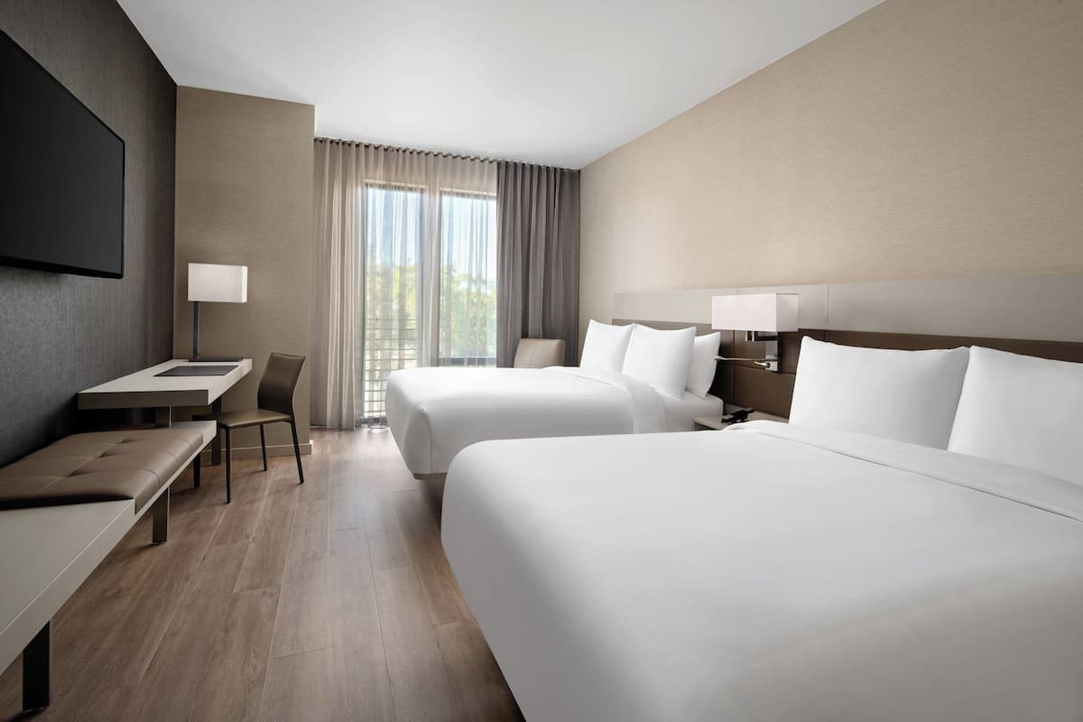 A hotel room with two beds, a desk, a chair, and a TV.