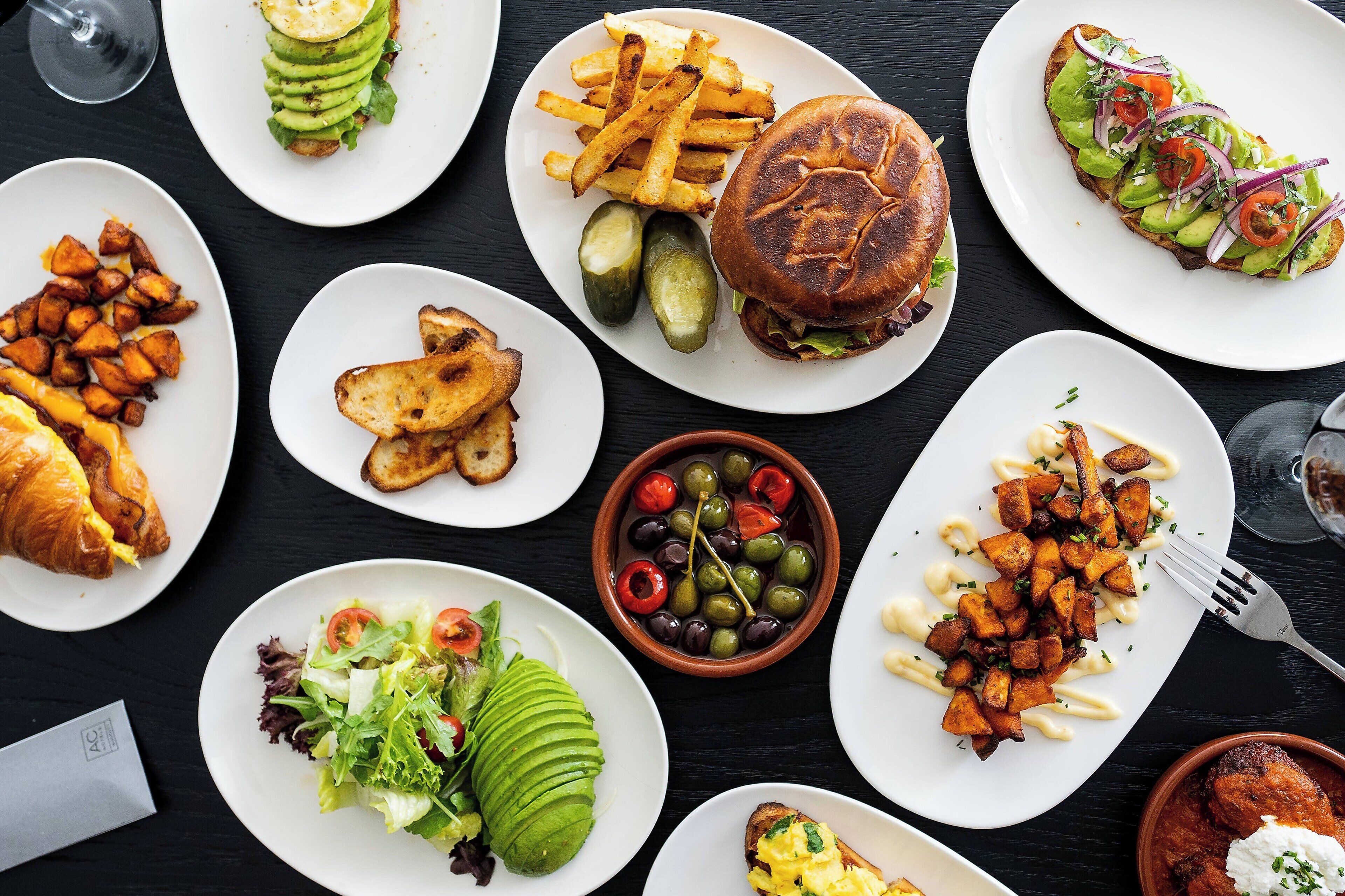A variety of dishes including a burger, fries, and a salad on a black table.