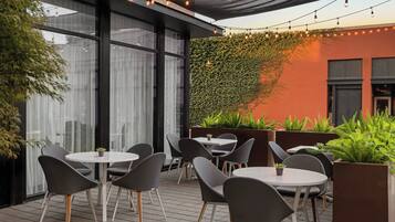 An outdoor seating area with round tables and chairs, a green wall with climbing plants, and string lights.
