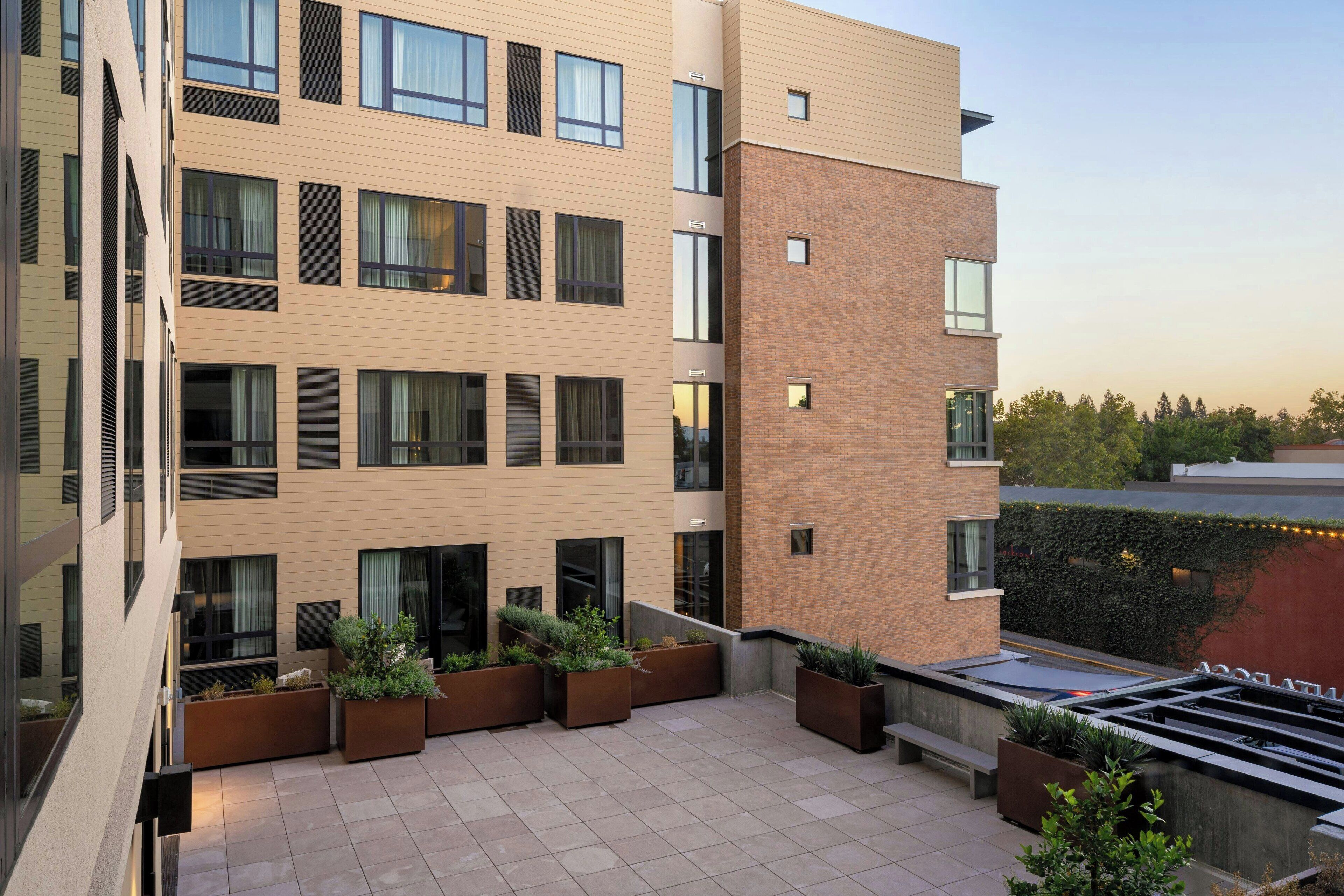 A modern building with multiple floors, large windows, and outdoor seating areas with planters.
