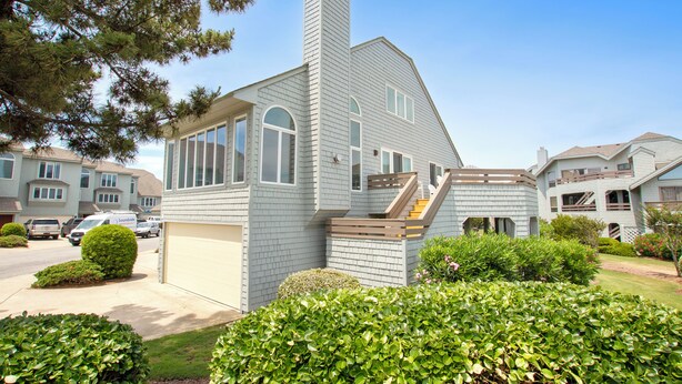 A two-story residential house with a garage, a chimney, and a well-maintained front yard with hedges and a lawn. - Oceanside, Hot Tub, Community Amenities, Close to beach, 665, Shore Beats Work (Corolla)