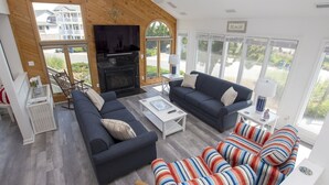 A modern living room with a fireplace, two sofas, a coffee table, and a striped chair. - Oceanside, Hot Tub, Community Amenities, Close to beach, 665, Shore Beats Work (Corolla)