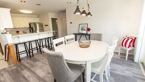 A modern kitchen with white cabinets, a stainless steel refrigerator, and a bar area with stools. - Oceanside, Hot Tub, Community Amenities, Close to beach, 665, Shore Beats Work (Corolla)