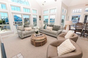 A spacious living room with large windows, a wicker coffee table, and a brown sofa. - Semi-Oceanfront, Private Pool, Ocean Views, Close to beach, BU76, Trading Winds (Corolla)