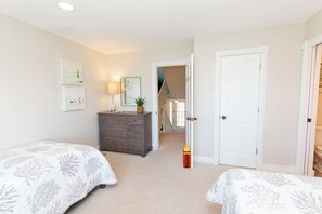 A bedroom with two beds, a dresser, and a door leading to a staircase.