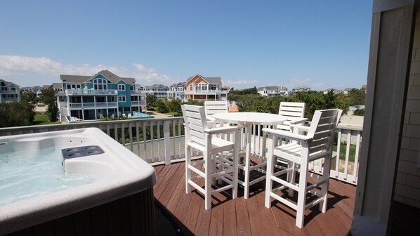A wooden deck with a hot tub and white chairs, overlooking a residential area with houses.