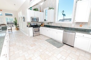 A modern kitchen with white cabinetry, stainless steel appliances, and a view of the beach.
