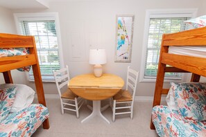 A room with bunk beds, a round table with chairs, a lamp, and a wall art piece.