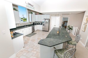 A modern kitchen with white cabinets, a granite countertop, and a view of the beach through the window. - Semi-Oceanfront, Private Pool, Ocean Views, Close to beach, BU76, Trading Winds (Corolla)