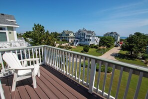 A wooden deck with a white chair, overlooking a residential area with houses and a clear sky. - Semi-Oceanfront, Private Pool, Ocean Views, Close to beach, BU76, Trading Winds (Corolla)