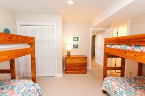 A bedroom with two bunk beds, a wooden dresser, and a door with louvered shutters.