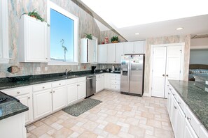 A modern kitchen with white cabinetry, a stainless steel refrigerator, and a large window with a view.