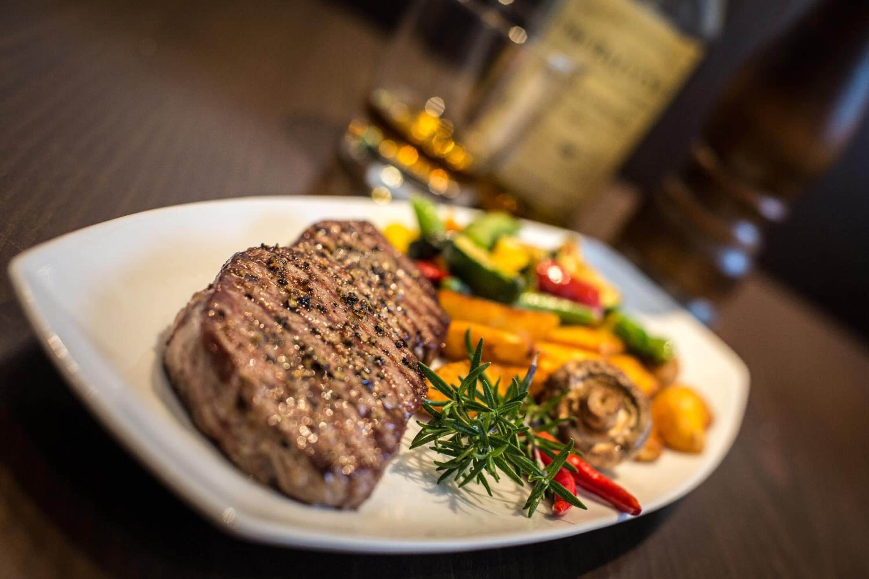 A plate with a steak, vegetables, and a sprig of rosemary.