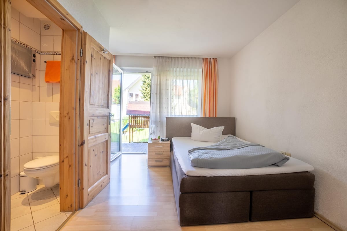 A bedroom with a bed, a wooden wardrobe, a toilet, and a shower area.