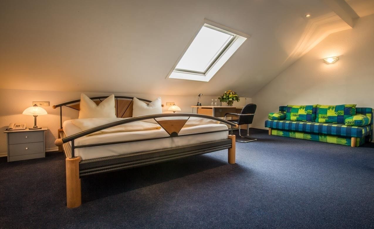 Ein Schlafzimmer mit einem Bett, einem Schreibtisch, einem Sessel, einer Couch und einem Oberlicht.
