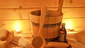 A wooden bucket with a wooden scoop, a bottle of bath salts, and towels on a wooden surface.