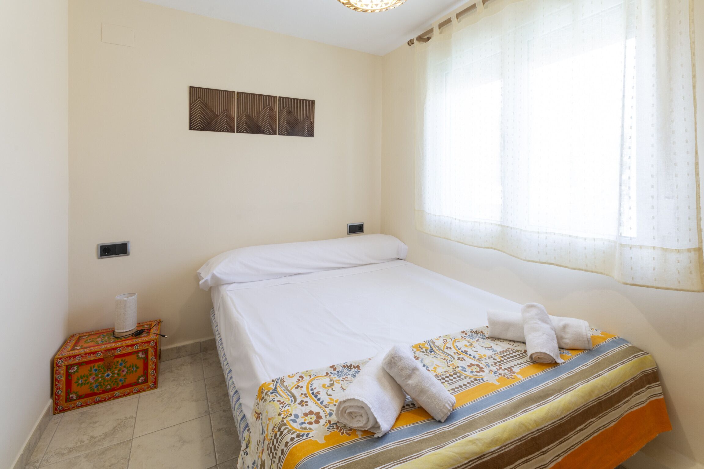 Una habitación de hotel con una cama, una mesita con una caja decorativa y una ventana con cortinas.