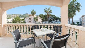 Un balcone con tavolo e sedie, vista su una zona costiera con edifici e palme.