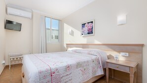 Un dormitorio con cama, mesita de noche, televisor de pared y ventana con cortinas.