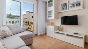 Una sala moderna con sofá, televisor y un balcón con vistas a edificios.