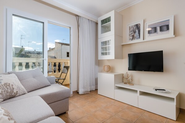 A modern living room with a sofa, TV, and a balcony with a view of buildings.