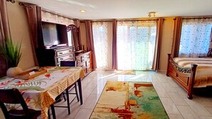 A hotel room with a bed, a desk with a chair, a television, a dresser, and a large window with curtains. - Spacious Waialua studio (Waialua)