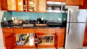 A kitchen with wooden cabinets, a stainless steel refrigerator, a sink, and a tiled backsplash. - Spacious Waialua studio (Waialua)