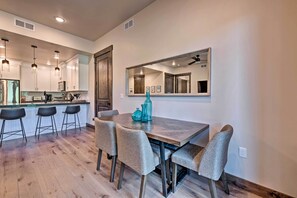 A modern kitchen with a wooden dining table, bar stools, and a large mirror above the table. - Luxe Canyons Condo w/ Golf Course Views! (Park City)