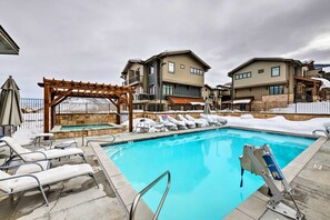A swimming pool with lounge chairs, a pergola, and a stone wall. - Luxe Canyons Condo w/ Golf Course Views! (Park City)