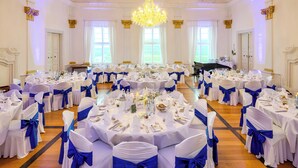 A banquet hall with round tables set for a formal event, featuring white tablecloths and blue sashes. - Schloss Horneck (Gundelsheim)