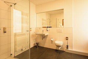 A modern bathroom with a glass shower enclosure, a sink with a mirror above it, and a toilet. - Schloss Horneck (Gundelsheim)