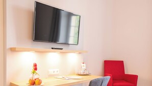 A modern room with a wooden desk, a red chair, a flat-screen TV mounted above the desk, and a vase with flowers on the desk. - Schloss Horneck (Gundelsheim)