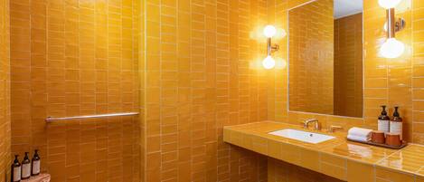 Un baño con paredes de azulejos amarillos, un lavamanos blanco y un espejo con iluminación.