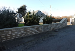 A stone wall with a sailboat design, a paved area, and a building with a sloped roof in the background.