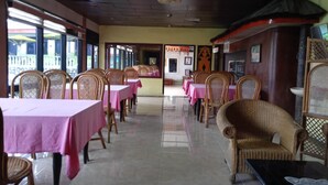 A restaurant with rows of tables and wicker chairs, a tiled floor, and a view through the open doorway. - OYO 2322 Dien Karona Hotel (Berastagi)