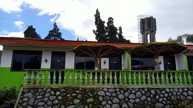 A building with a green facade, stone wall, and a balcony with green balustrades. - OYO 2322 Dien Karona Hotel (Berastagi)