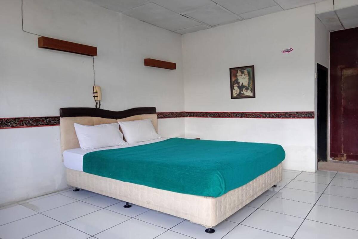 Quarto individual com uma colcha verde-turquesa, roupa de cama branca e uma moldura de parede estampada.