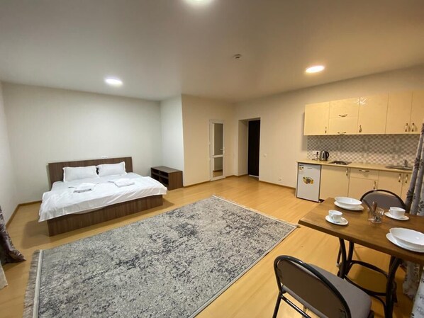 A compact room with a bed, a dining table with chairs, a small kitchen area, and a bathroom.
