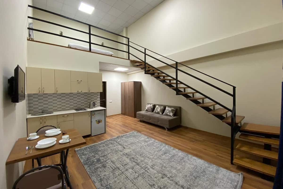 A compact living space with a kitchenette, a dining area, a sofa, and a staircase.