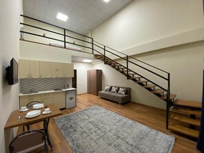 A compact living space with a kitchenette, a dining area, a sofa, and a staircase.
