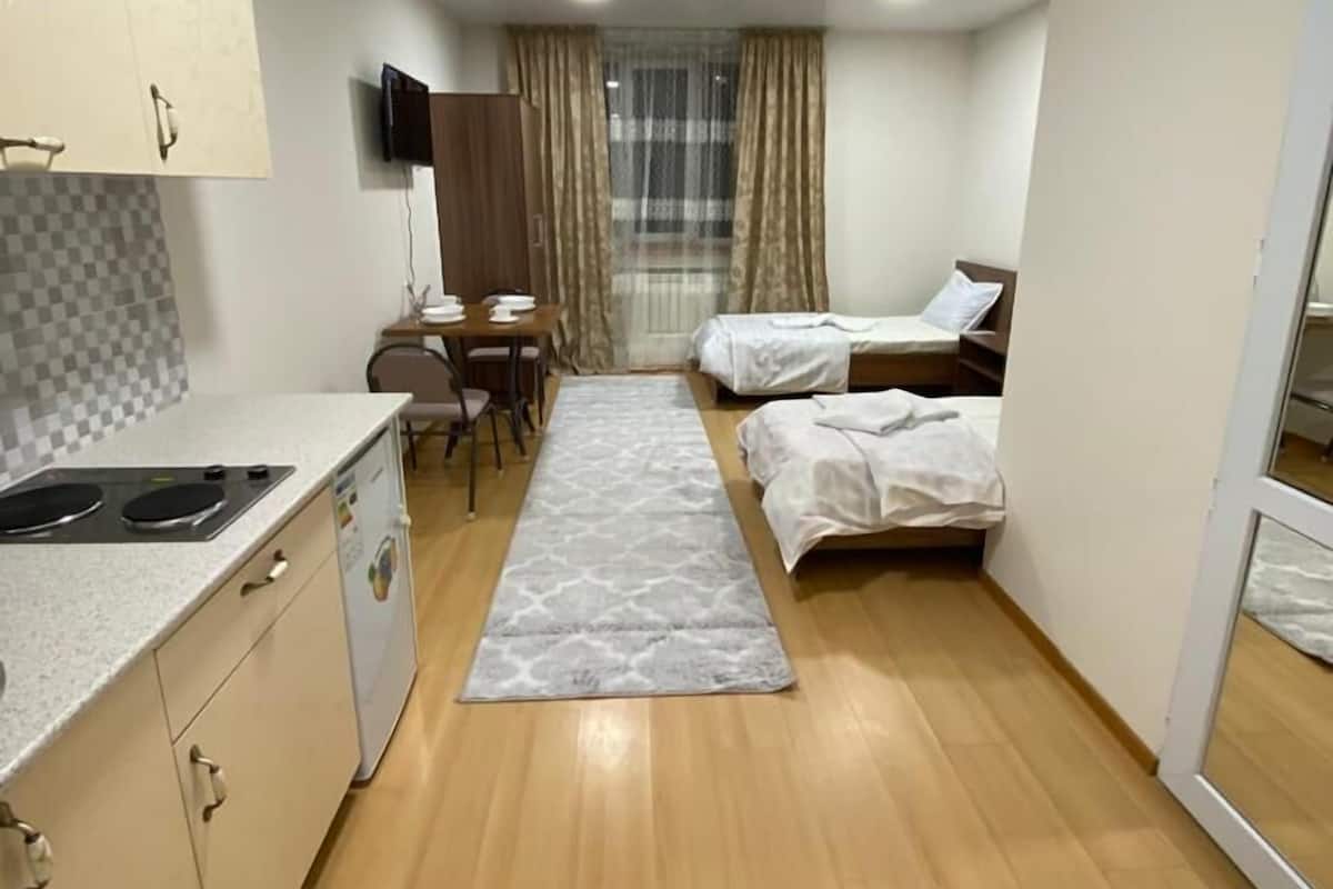 A compact hotel room with a kitchenette, a single bed, a small table, and a TV.