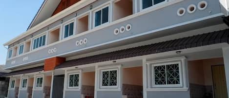 Un edificio residencial de varios pisos con balcones, ventanas grandes y techo de tejas.