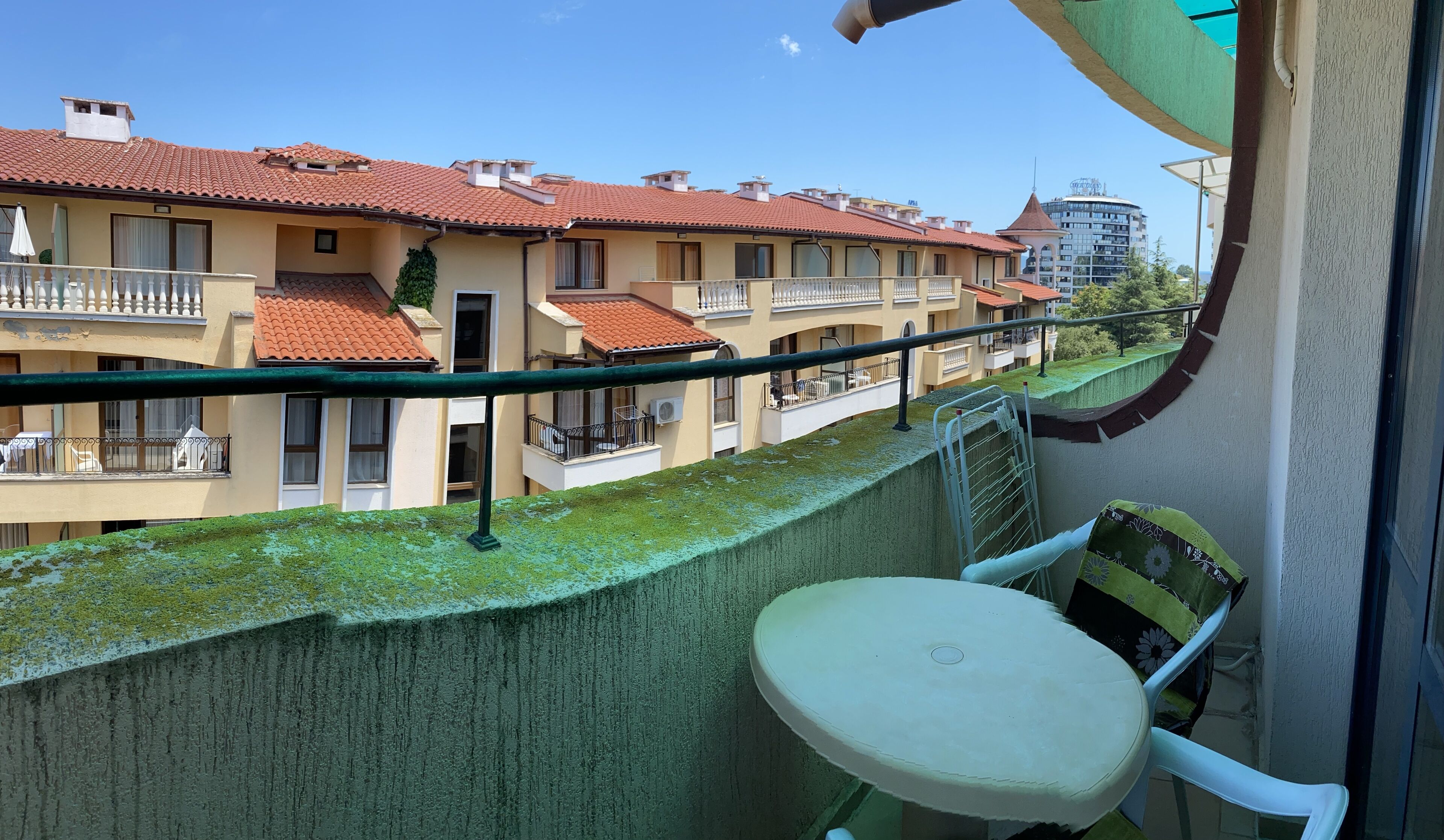 A balcony with a table and chairs, overlooking a row of terraced houses with red-tiled roofs.
