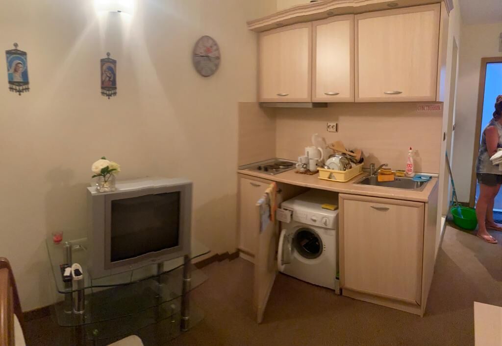A compact kitchen with a washing machine, a small sink, and a television.